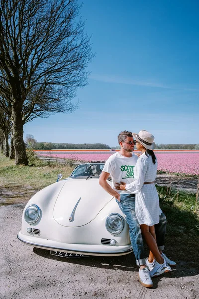 Lisse Netherlands,. пара, путешествующая со старым винтажным спортивным автомобилем White Porsche 356 Speedster, Голландская цветочная луковица область с тюльпановыми полями — стоковое фото