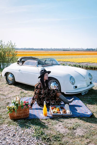 Lisse Netherlands,. casal fazendo uma viagem com um velho carro esporte vintage Branco Porsche 356 Speedster, holandês região bulbo flor com campos de tulipa — Fotografia de Stock