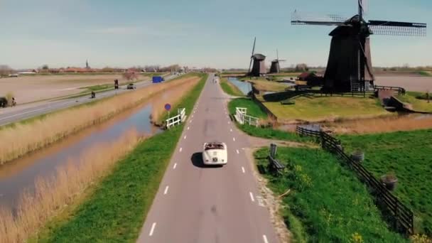 Schermerhorn Alkmaar Países Baixos,. casal fazendo uma viagem com um velho carro esporte vintage Branco Porsche 356 Speedster, aldeia moinho holandês Schermerhorn — Vídeo de Stock