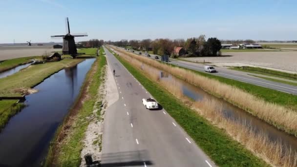 Schermerhorn Alkmaar, Netherlands 2020 년 4 월. 부부가 오래 된 빈티지 스포츠카 White Porsche 356 Speedster, Dutch windmill village Schermerhorn 과 함께 도로 여행을 하고 있다. — 비디오