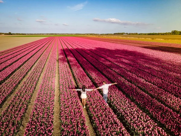 Pareja de hombres y mujeres en el campo de flores en los Países Bajos durante la primavera, campo de tulipanes rojos anaranjados cerca de Noordoostpolder Flevoland Países Bajos, hombres y mujeres en el sol de la noche de primavera — Foto de Stock