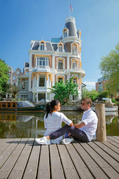 Pareja en un viaje a Ámsterdam, hombres y mujeres relajándose junto a los canales de Ámsterdam durante la primavera 2020 abril en Europa Países Bajos — Foto de Stock