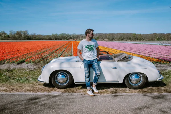 Lisse Holandia. para robi wycieczkę ze starym zabytkowym samochodem sportowym White Porsche 356 Speedster, holenderski region kwiatowy żarówki z polami tulipanów — Zdjęcie stockowe