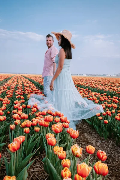 Paar mannen en vrouwen in bloemenveld in Nederland in het voorjaar, oranje rood tulpenveld bij Noordoostpolder Flevoland Nederland, mannen en vrouwen in de lenteavond zon — Stockfoto