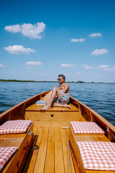 Los hombres de Giethoorn Netherlands visitan el pueblo con un barco, vista del famoso pueblo con canales y casas rústicas con techo de paja en la zona agrícola en un día caluroso de primavera — Foto de Stock