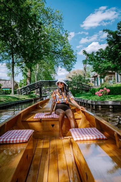 Giethoorn Países Bajos mujer visita el pueblo con un barco, vista de la famosa aldea con canales y casas de techo de paja rústica en la zona de la granja en un día de primavera caliente — Foto de Stock