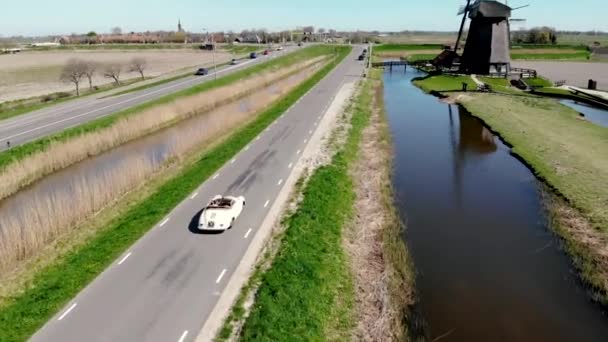 Schermerhorn Alkmaar Holandia kwiecień 2020,. para robi wycieczkę ze starym zabytkowym samochodem sportowym White Porsche 356 Speedster, holenderska wioska wiatrak Schermerhorn — Wideo stockowe