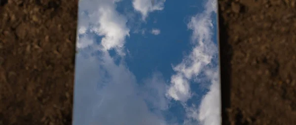 The cloudy sky seen reflected in a mirror that is on the ground