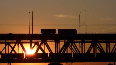 Gün batımında köprüden geçen bir kamyonun silueti.