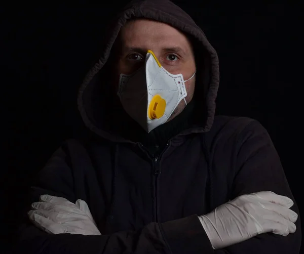 calm man with arms crossed on chest in a hood, sterile gloves and white antiviral mask isolated on a black background