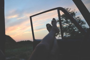 Rahatlayan genç adam bacak bacak bacak üstüne atmış bir fotoğrafını çekiyor. Gün batımında klasik araba kapısının açık penceresinde açıkta.