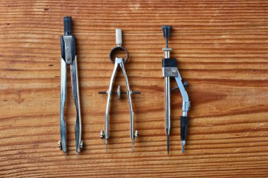 Ahşap zemin üzerinde izole edilmiş iki metal bölme ve bir metal çizim pusulayı içeren çizim araçlarının yakın çekim seti