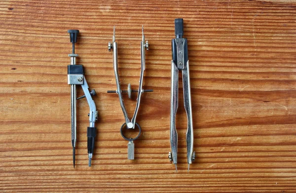close-up of set of drawing tools including two metal dividers and one metal drawing compass isolated on wooden background