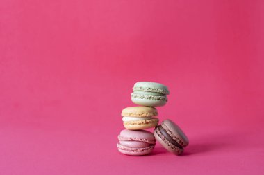 Pembe arka planda parlak renkli, üst üste yığılmış Fransız makarnaları