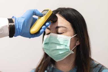 Bir doktor lazer termometreyle hastanın alnının sıcaklığını ölçer. Salgın virüs salgını kavramı