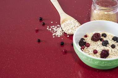 Yulaflı yoğurt ve ahşap kaşığın yanında kırmızı meyveler ve keten kavanozla.