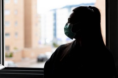 Genç ve ciddi bir kadının tıbbi koruyucu maske taktığı profiline yakın plan. Odaklanmamış bir arka plan ve metin için bir kopya alanı var. COVID-19 dünya çapında bulaşıcı salgın hastalıkların önlenmesi kavramı