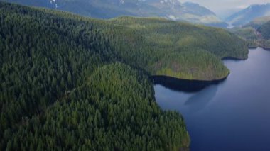 Kristal berrak mavi göl ve yeşil çam ağaçlarıyla çevrili tepeler.