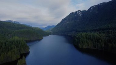 Güneşli bir günde, yeşil ormanla dağların arasındaki gölün mavi suyu.