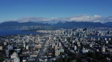 Güneşli bir günde Vancouver şehir merkezindeki hava manzarası. Arkasında görünür dağlar ve anakaraya bağlı köprüler var.