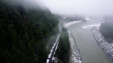 Demiryolunun üzerinden bir tarafta yavaşça akan nehirle diğer tarafta yeşil dağ ormanıyla uçun.
