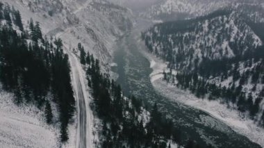 Nehirde yüzen buz manzarası ve etrafındaki büyük dağlar ve kış boyunca küçük bir yol.
