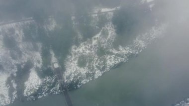 Nehir kıyısının yukarıdan görünen manzarası hafif kar ve nehri geçen köprü ile kaplı.