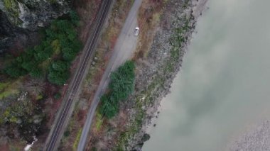 Dağların ve nehrin kıyısındaki demiryolu manzarası.