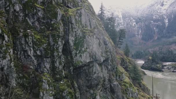 カナダの雪で覆われた川と山の後ろに岩の多い山の近くで飛行ショットを閉じる — ストック動画