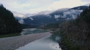 Hızlı akan bir nehir ve arka planda karla kaplı dağ tepeleriyle vadiden uç.