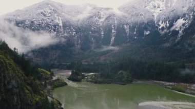 Nehrin üzerinden uç ve tüneli olan kayalık bir dağ. Arka planda karlı orman dağları