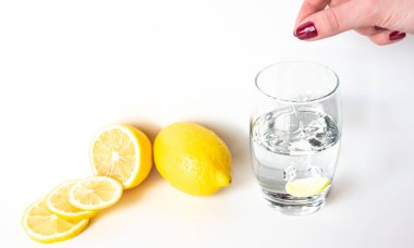 Kız, C vitamini hapını bir bardak suya batırıyor. Yakınlarda limon var.