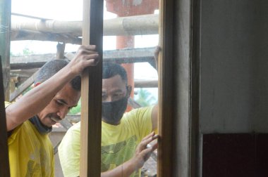 Endonezya 'da. 01 Mayıs 2020. Maskeli iki adam eski evi tamir ediyor.