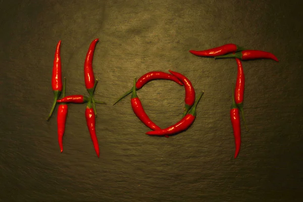 Photography of red hot peppers set on "hot" word shape on slate — 스톡 사진