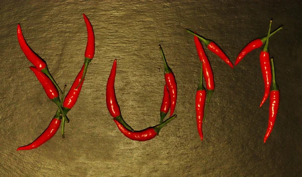 Photography of red hot peppers set on "yum" word shape on slate — 스톡 사진
