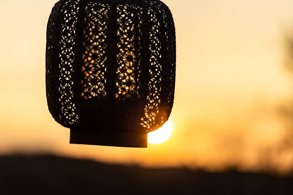 hand holding oriental lantern with candle while sunset. Sun is shining through the lamp.