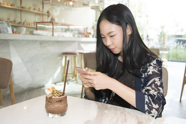 Mujer asiática mensajes de texto en el teléfono inteligente cuando se sienta en el café —  Fotos de Stock