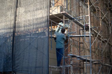 Sıvacı tuğlayla harç hazırlamak için iskeleye tırmanıyor. 