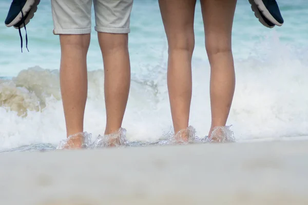 Cariño pareja piernas de pie contra la ola sobre la playa y whit — Foto de Stock