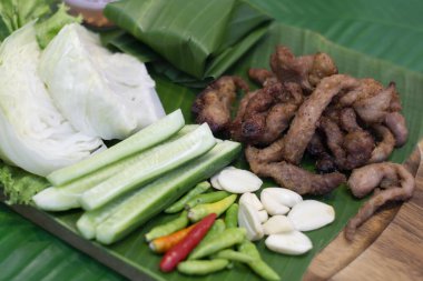 Kızarmış domuz eti, sarımsaklı ve biberli taze sarımsak, kırmızı biber, salatalık, muz yaprağının üzerinde lahana..