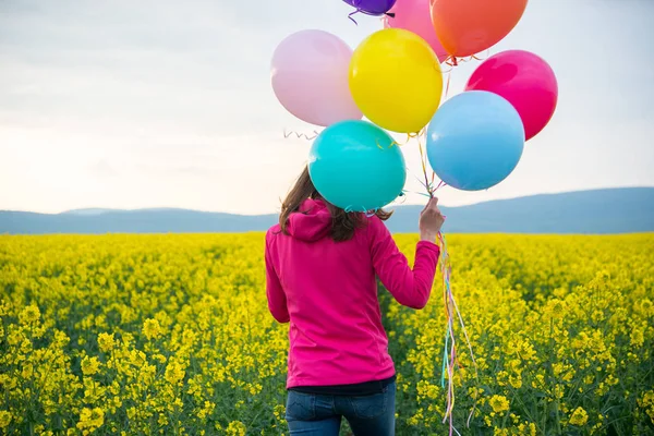 Beautiful woman with colorful balloons in field — Stock Photo, Image