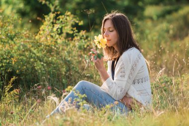 Güzel bir kadın sarı gülle tarlada oturuyor.