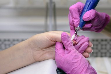 Pembe eldivenli manikürcü çeşitli ekipmanlarla yetişkin bir müşterinin tırnaklarını inceliyor. Manikür. Güzellik salonu. Eldivenli eller ellerin tırnaklarıyla ilgilenir. Prosedür.