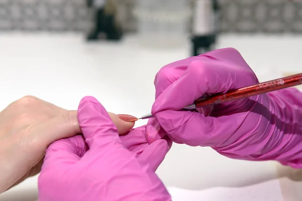 Manicurist in pink gloves processes the nails of an adult client using a variety of equipment. Manicure. Beauty shop. Gloved hands take care of the nails of the hands. Procedures.