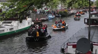 Amsterdam, Hollanda - 28 Nisan 2018: Teknedeki insanlar Hollanda 'nın Amsterdam şehrinde Kral gününü kutluyorlar. Kralın günü Hollanda Krallığı 'nda ulusal bayramdır. İnsanlar Amstel nehir kanalında kayıklara biniyor.