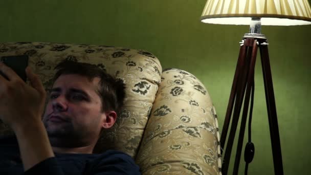男子在入睡前在沙发上阅读智能手机. — 图库视频影像