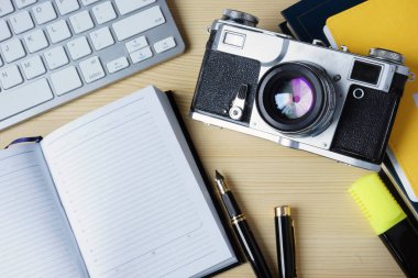 Açık not defteri, klavye ve vintage fotoğraf makinesi üzerinde bir ahşap des