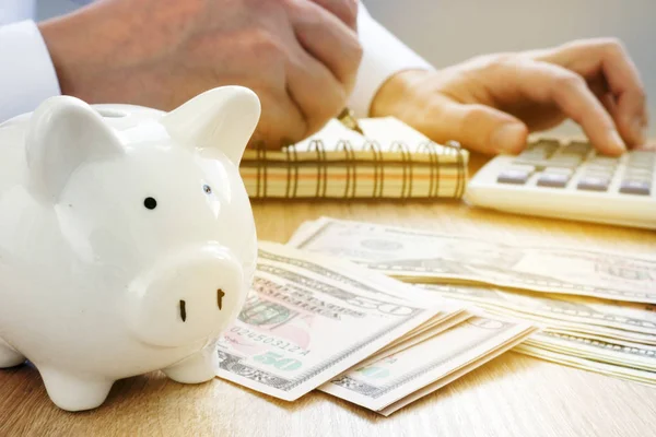 Hombre escribiendo en un libro de contabilidad, alcancía y billetes de dólar. Concepto de ahorro . — Foto de Stock