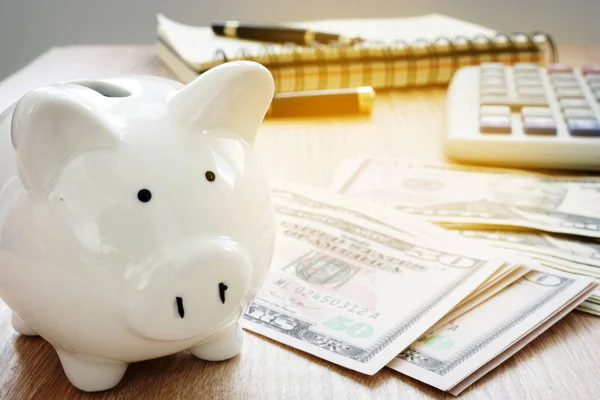 Ahorro o concepto de presupuesto para el hogar. Calculadora, billetes de dólar y alcancía . — Foto de Stock