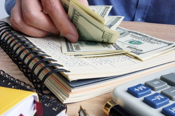 Mann, der Dollarscheine zählt. Schreibtisch mit Taschenrechner, Buch und Dollars. — Stockfoto